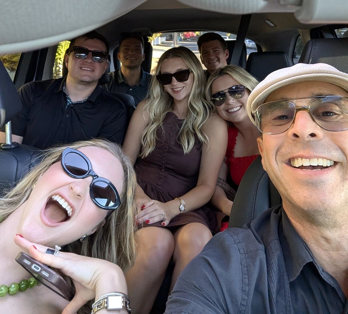 Group of seven smiling wine tour guests laughing together inside a car on the way to Edna Valley wineries