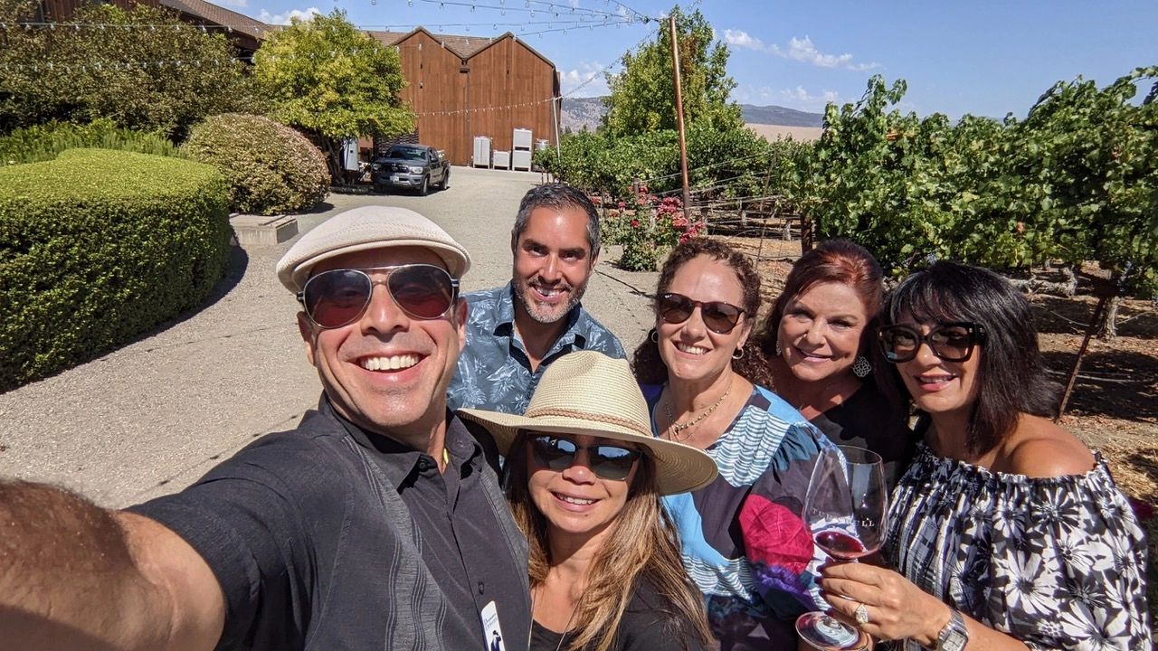 Five smiling wine tour guests taking a selfie with a glass of red wine at a Temecula Valley winery